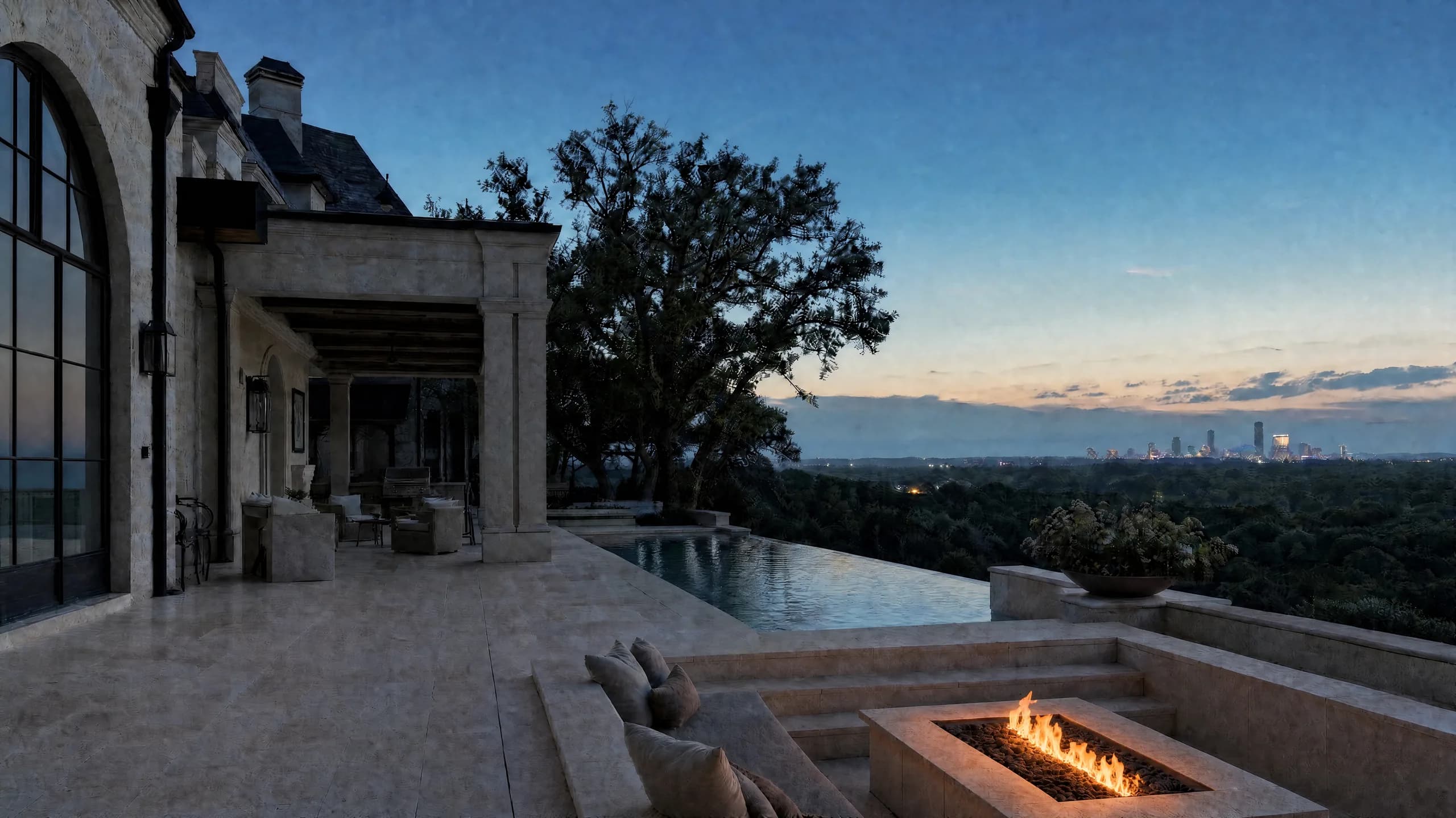 Limestone terrace at dusk with a low linear fire, an infinity pool, and a distant city skyline beyond a wooded valley