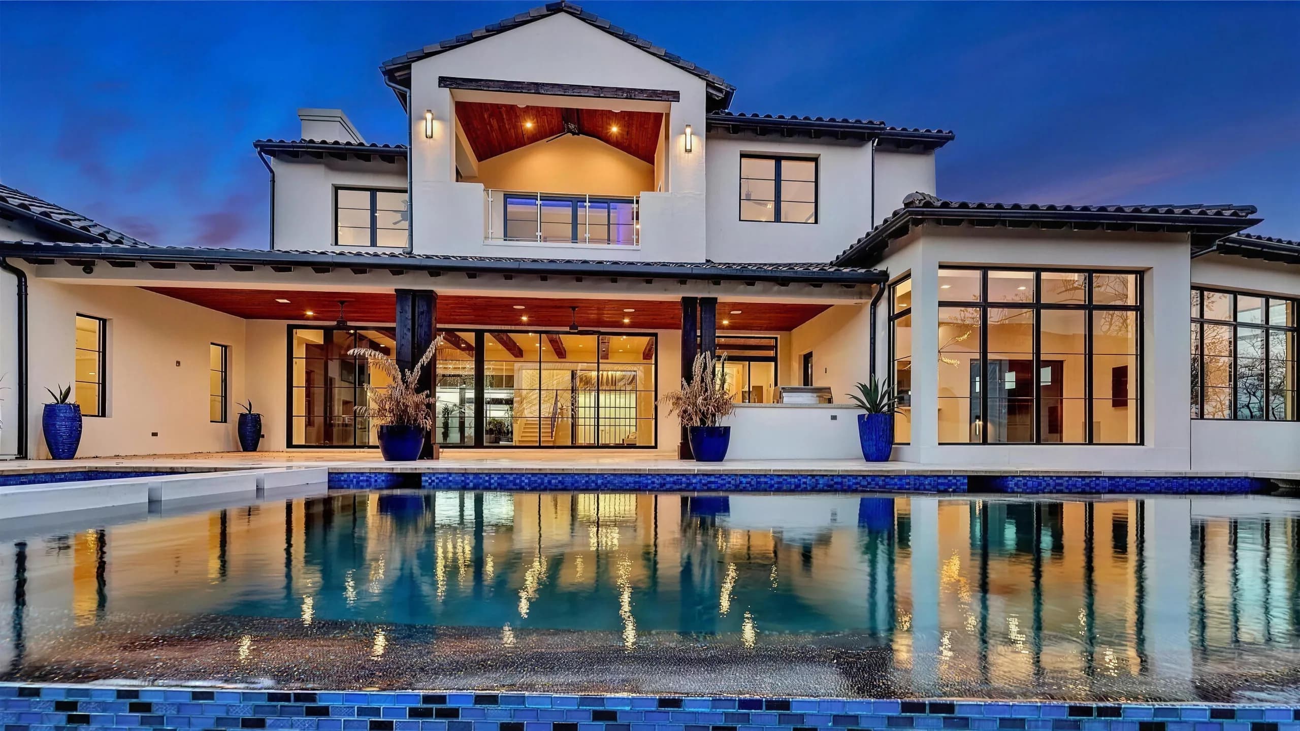 The rear of the home seen straight on across the pool at dusk, its floor-to-ceiling steel windows lit and reflected in the water